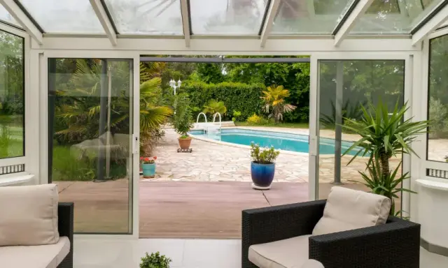 Une extension vitrée moderne s'ouvre sur une piscine et un jardin luxuriant, invitant à la détente.