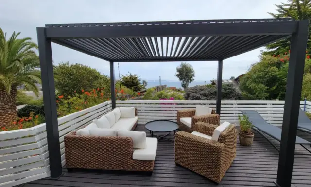 Un salon d'extérieur confortable sous une pergola sur toit terrasse, avec vue sur la mer.