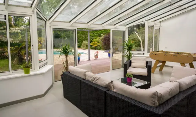 Vaste veranda 50m2 avec salon, baby-foot et vue sur piscine. Idéal pour se détendre et s'amuser en famille.
