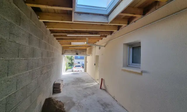 Couloir en construction, partie d'une extension maison, avec murs en parpaings, plafond en bois, fenêtre de toit et matériaux de chantier.