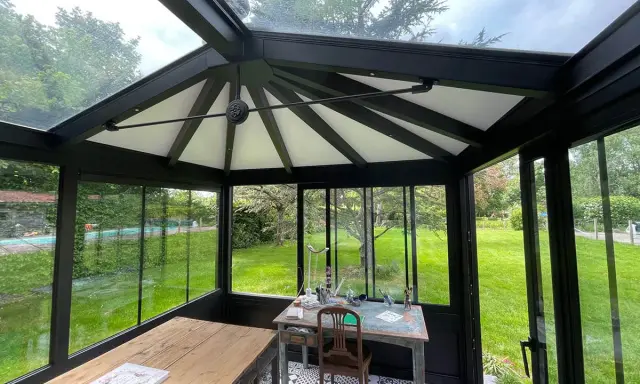 Intérieur d'une **veranda 2 pans** avec mobilier, sol décoratif et vue sur un jardin verdoyant.