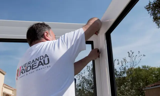 Un ouvrier installe une structure de véranda, remplaçant un ancien surbau béton.