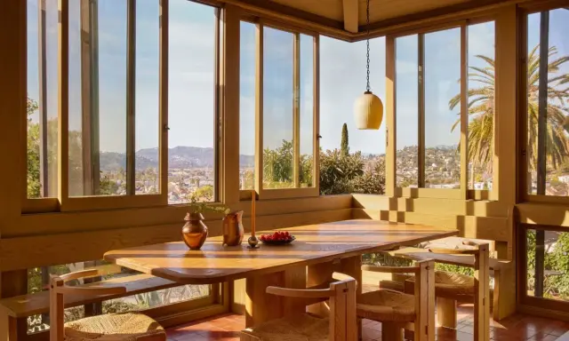 Une salle à manger lumineuse dans une veranda sur terrasse en bois, avec vue panoramique sur la ville et les palmiers.