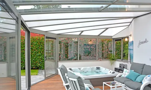 Une **fenêtre de toit veranda** lumineuse abrite un jacuzzi et un coin salon confortable, avec vue sur un jardin luxuriant.