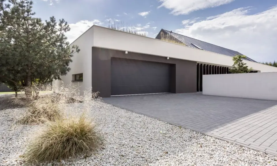 Moderne maison avec agrandissement garage, allée pavée, gravier blanc et végétation.