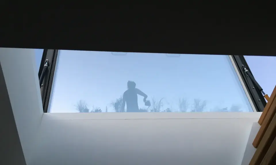 Silhouette d'une personne arrosant des plantes à travers un puit de lumière panneau sandwich.