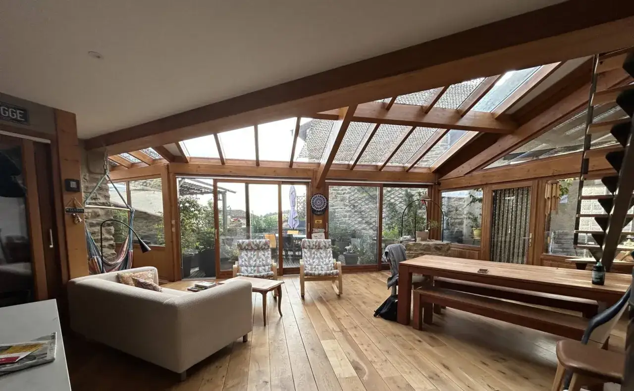 Vaste extension bois avec salon, salle à manger et vue sur jardin. Lumière naturelle abondante grâce au toit vitré.