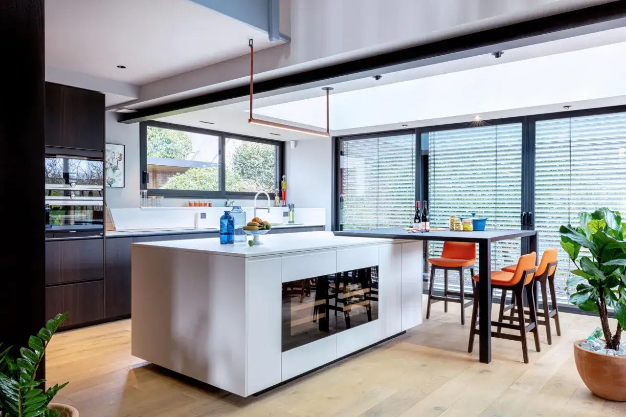 Cuisine moderne avec &icirc;lot central et banquettes, s'ouvrant sur un jardin verdoyant. Une extension cuisine sur jardin lumineuse et spacieuse.