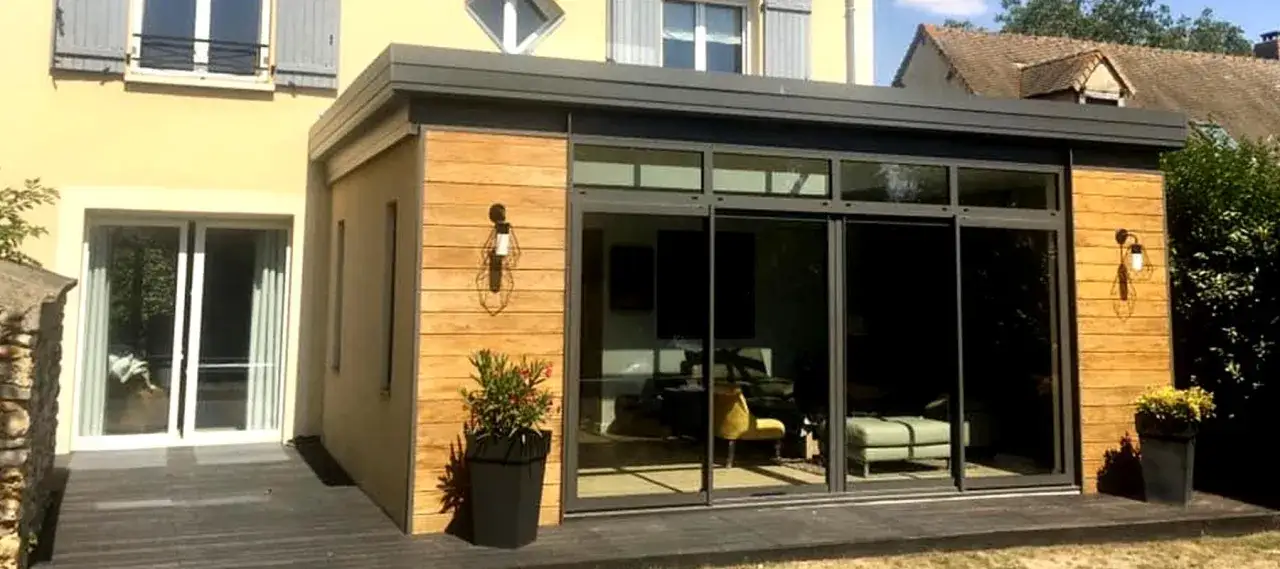 Agrandissement maison sur le côté avec murs en bois et grandes baies vitrées donnant sur un salon moderne.