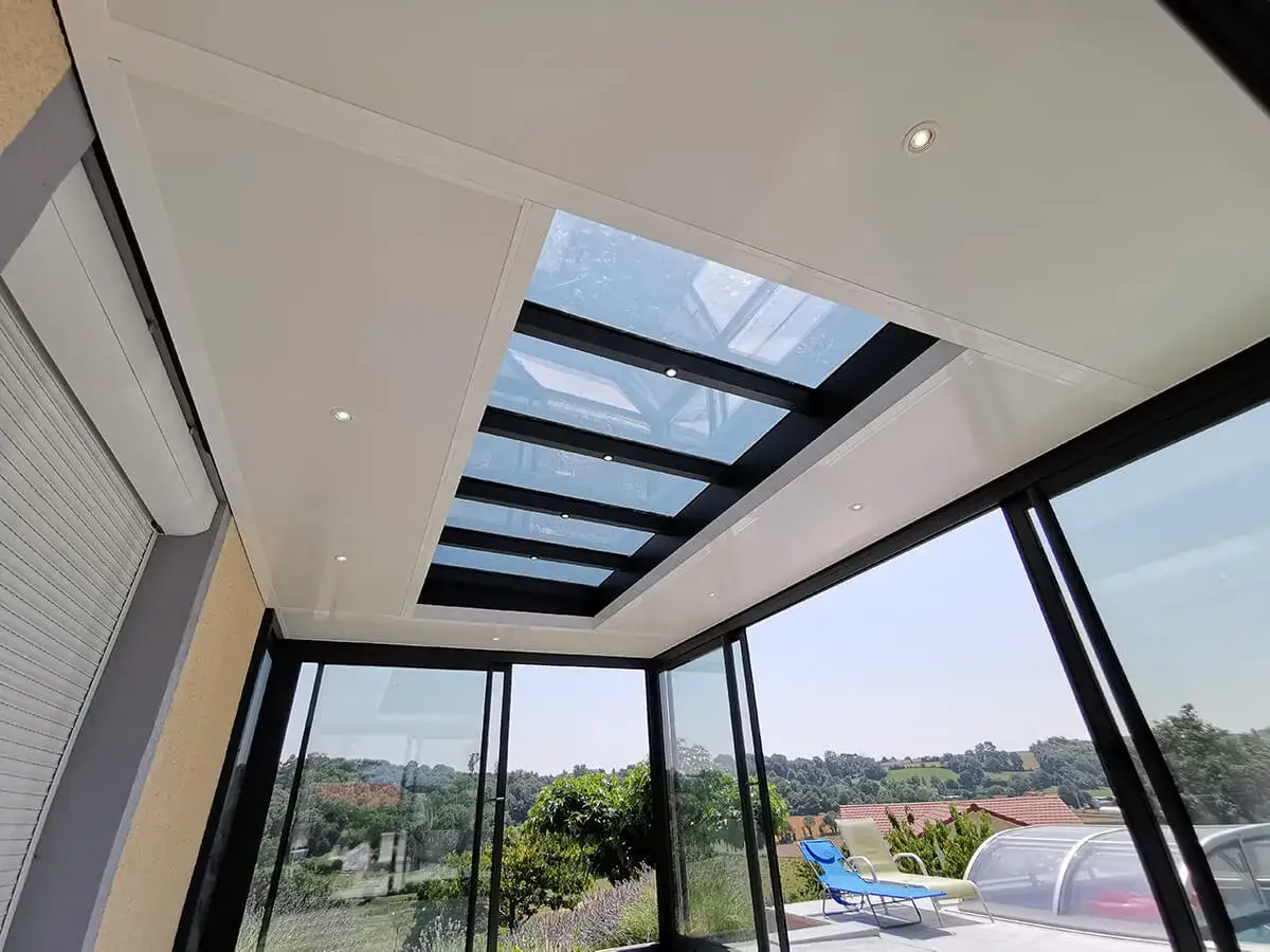 Verri&egrave;re moderne avec toit plat en bac acier, baignant l'espace de lumi&egrave;re naturelle. Des spots int&eacute;gr&eacute;s &eacute;clairent la pi&egrave;ce.