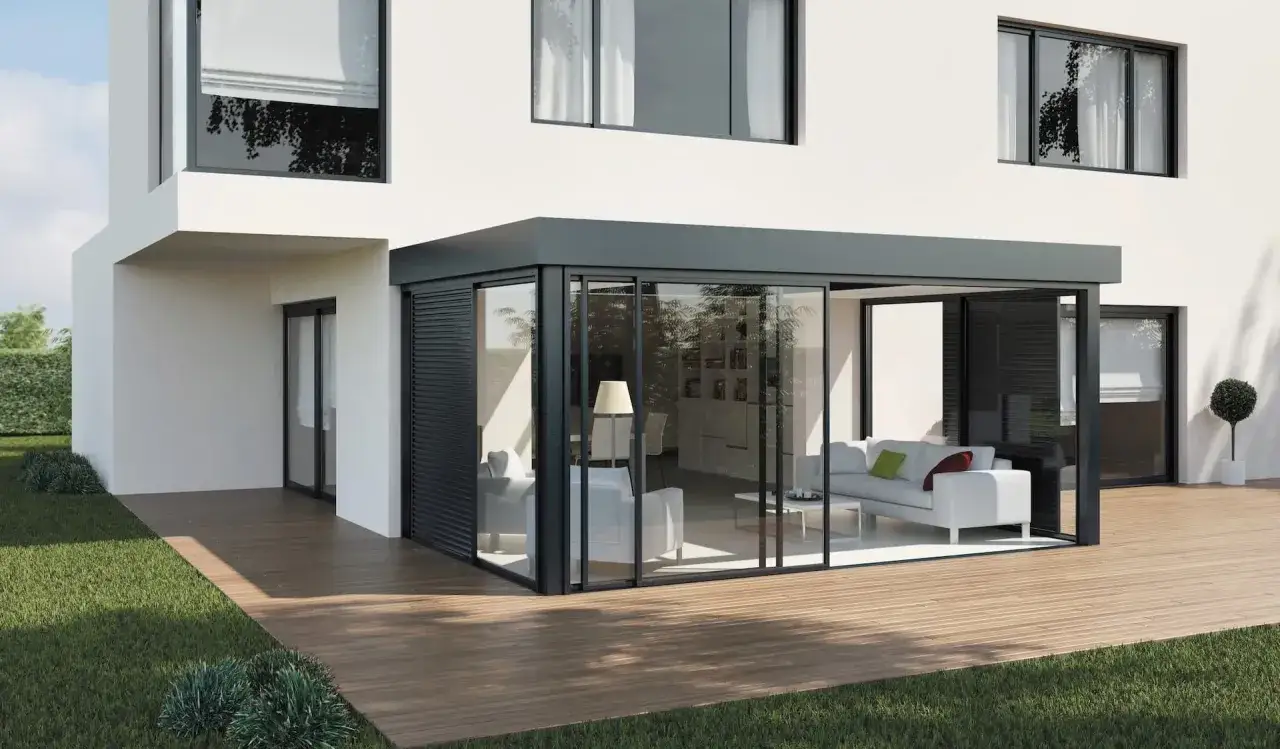 Une veranda moderne, con&ccedil;ue par un architecte, s'ouvre sur une terrasse en bois. L'int&eacute;rieur est lumineux avec un canap&eacute; blanc.