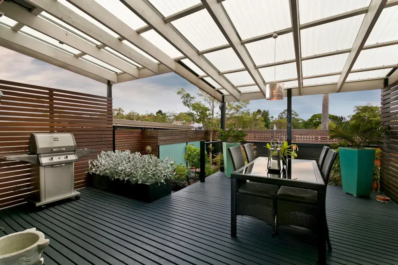 Terrasse moderne avec barbecue, table et chaises sous une pergola. Le sens de pose de canisse sur pergola est bien visible, offrant ombre et intimit&eacute;.