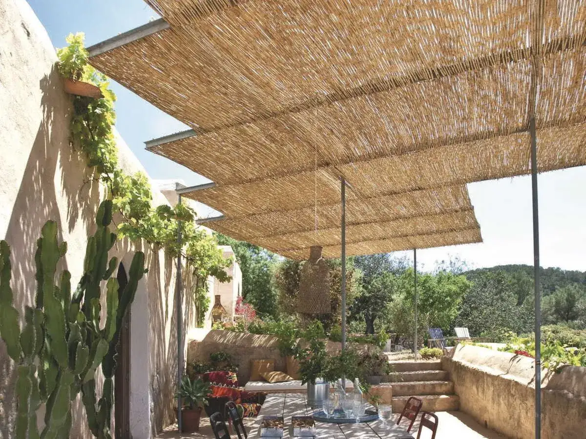 Une pergola bois canisse offre une ombre naturelle et chaleureuse &agrave; cette terrasse m&eacute;diterran&eacute;enne, orn&eacute;e de cactus et de v&eacute;g&eacute;tation luxuriante.
