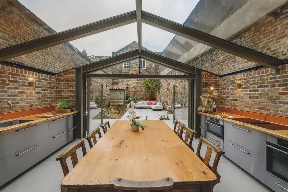 Une cuisine moderne avec une extension vitrée toit plat, donnant sur un jardin avec salon de jardin.