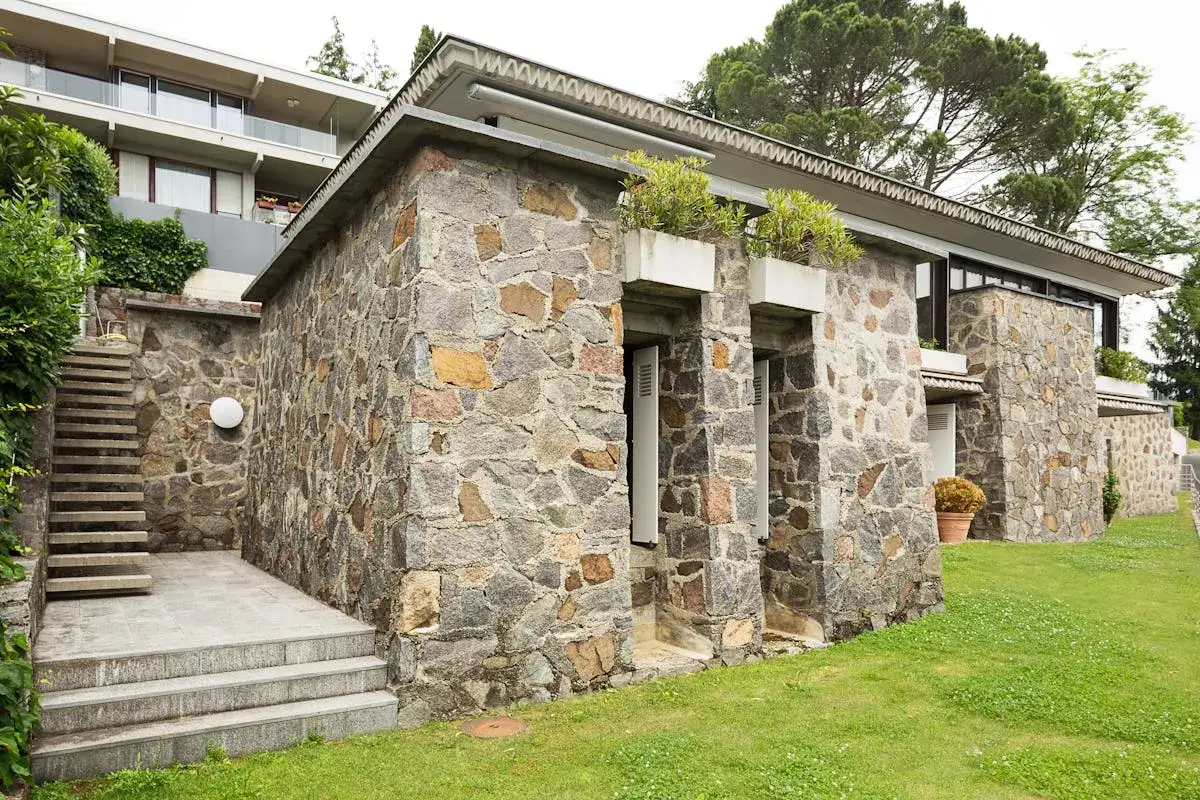 Maison en pierre avec extension moderne. Un escalier mène à une partie de la maison en pierre brute, contrastant avec la partie supérieure plus claire.