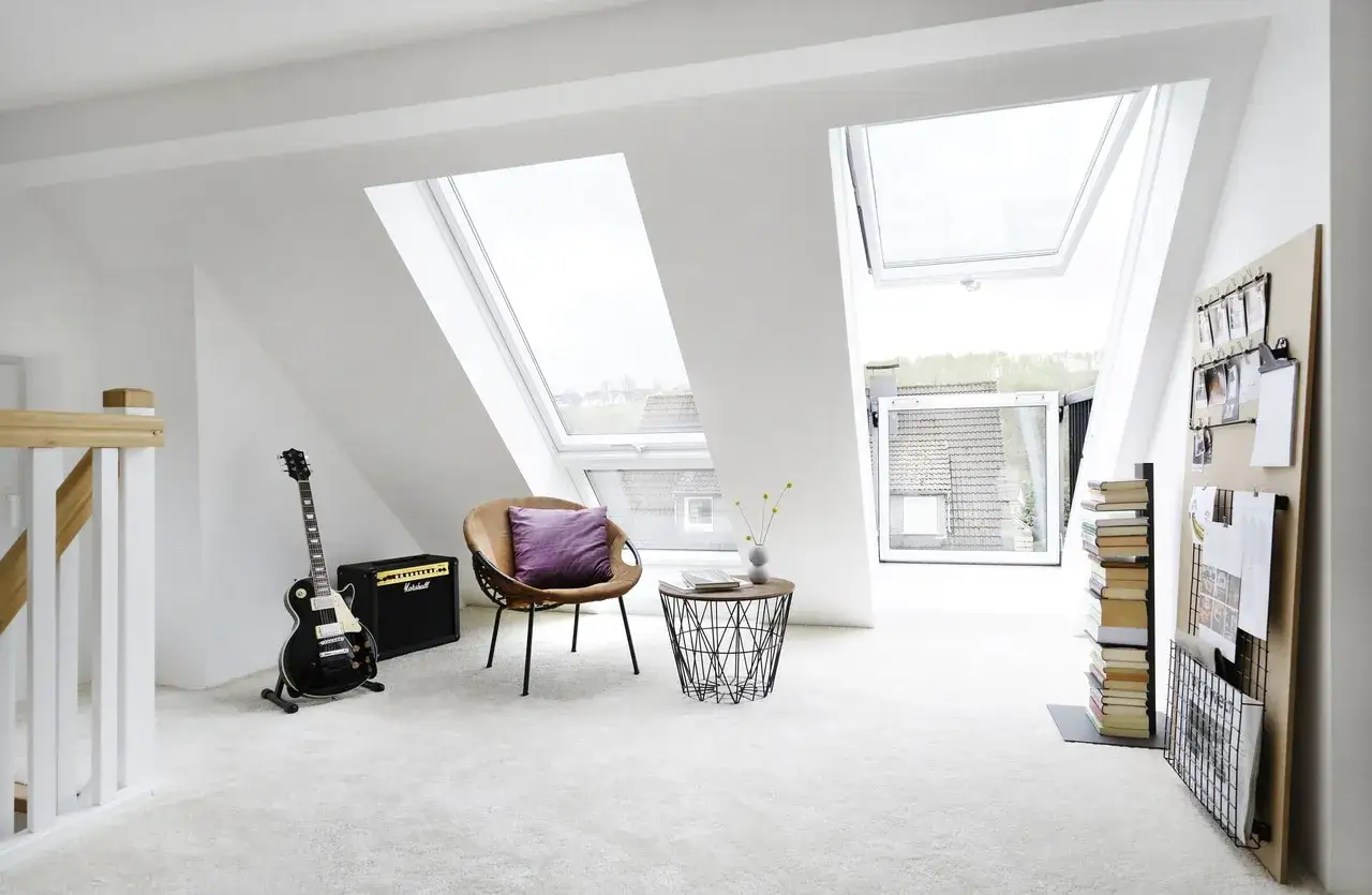 Un coin musique sous un puit de lumière, avec une guitare, un ampli, un fauteuil confortable et une étagère remplie de livres.