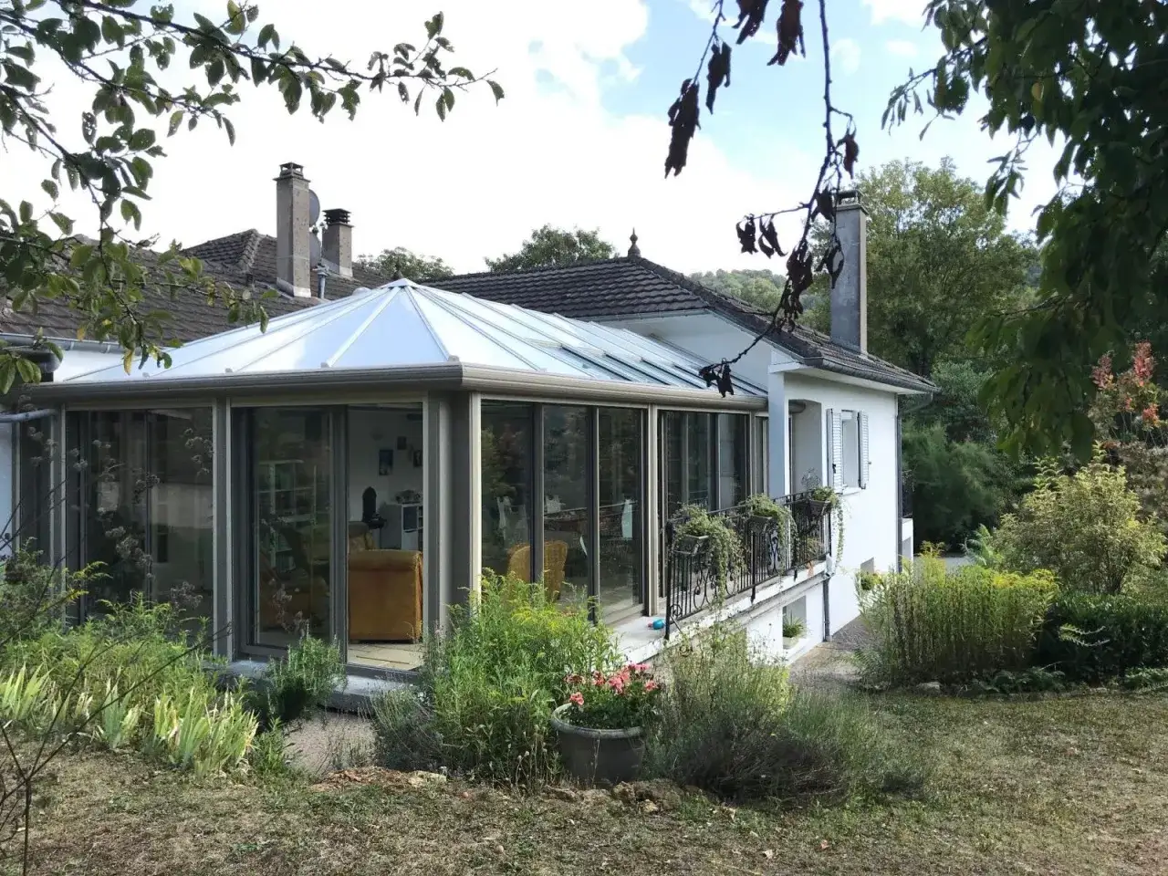 Une maison avec une v&eacute;randa 2 pans lumineuse, entour&eacute;e d'un jardin verdoyant.