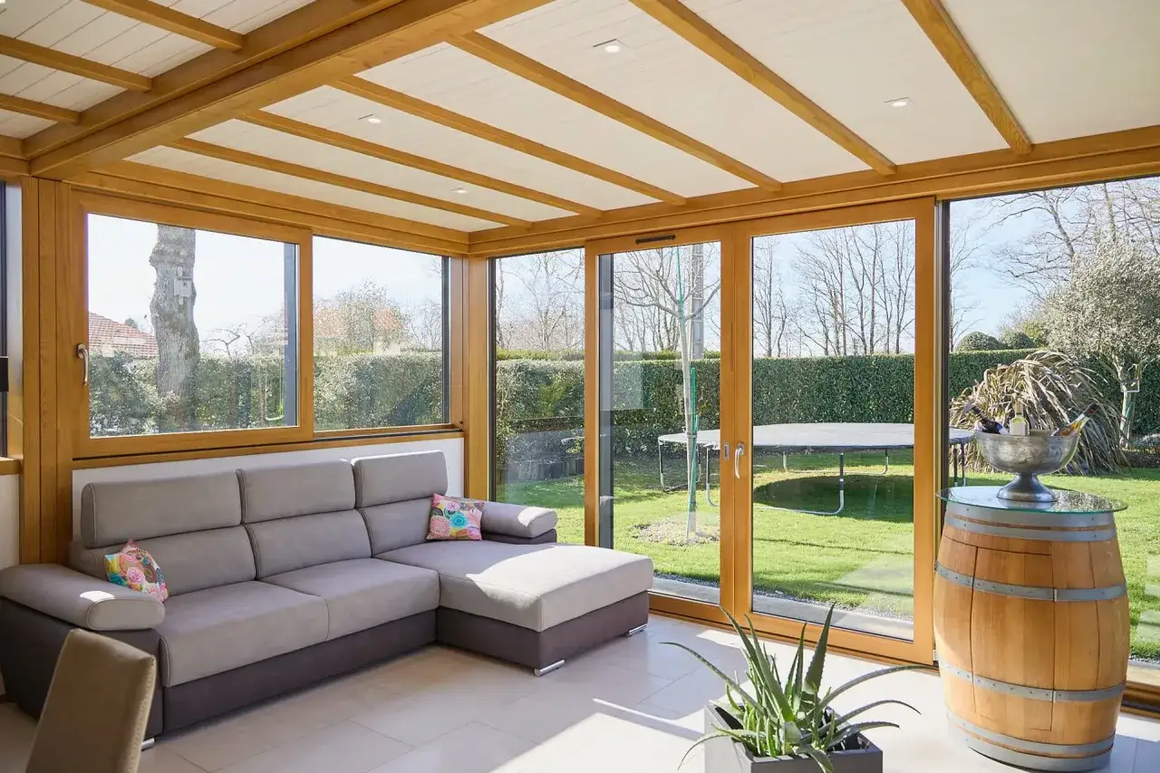 Un canapé confortable dans une veranda lumineuse avec vue sur une terrasse et un jardin verdoyant.