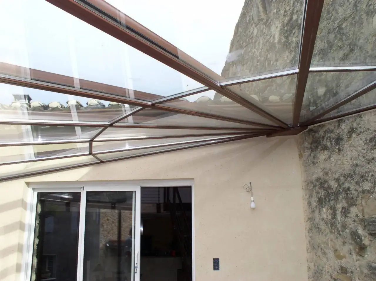 Veranda d'angle d'une maison, avec une structure vitr&eacute;e moderne et une partie en pierre ancienne.