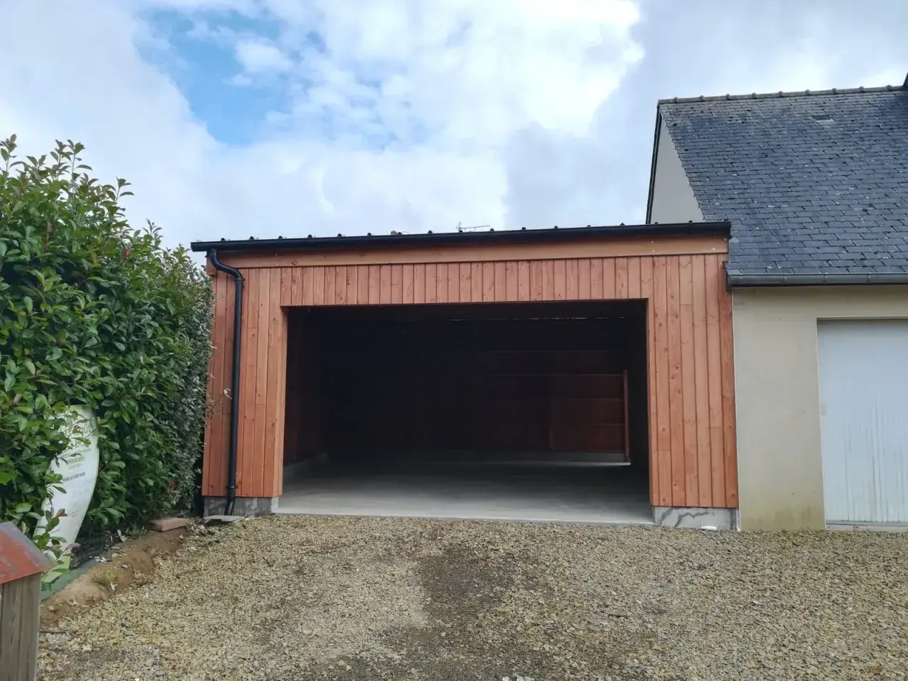 Extension garage bois accolé maison, avec une grande ouverture et un toit plat.