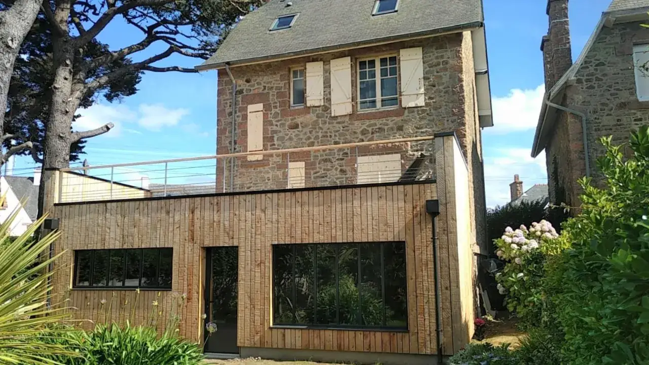 Maison en pierre avec extension bois moderne. Une extension toit terrasse accessible offre un espace extérieur supplémentaire.