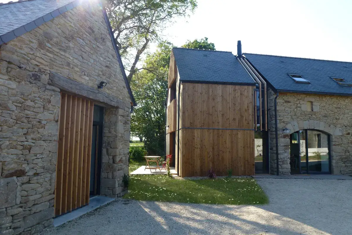 Extension d'une maison ancienne en pierre et bois, avec une partie moderne en bardage bois et des ouvertures vitr&eacute;es.