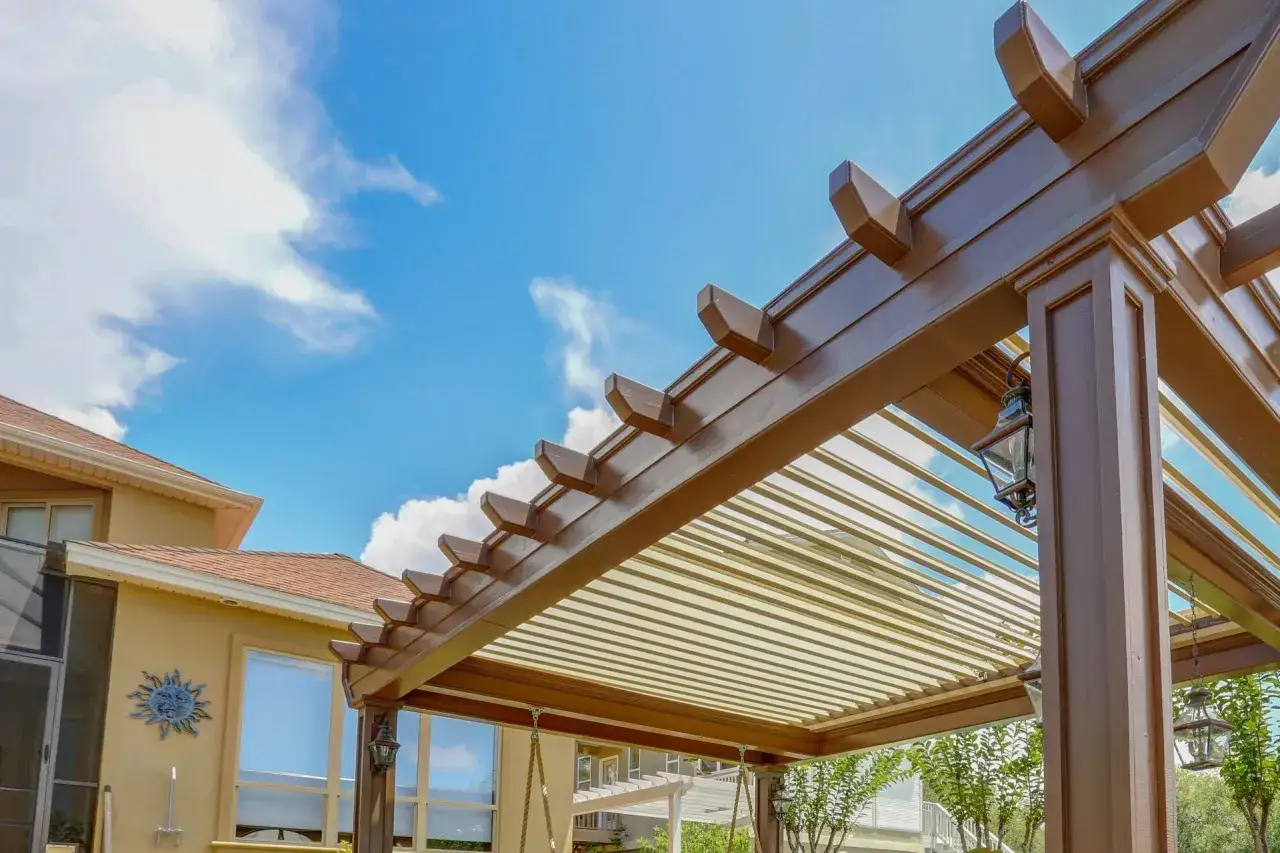 Un ciel bleu avec des nuages blancs au-dessus d'une pergola en bois brun, parfaite pour couvrir une terrasse et profiter de l'extérieur.
