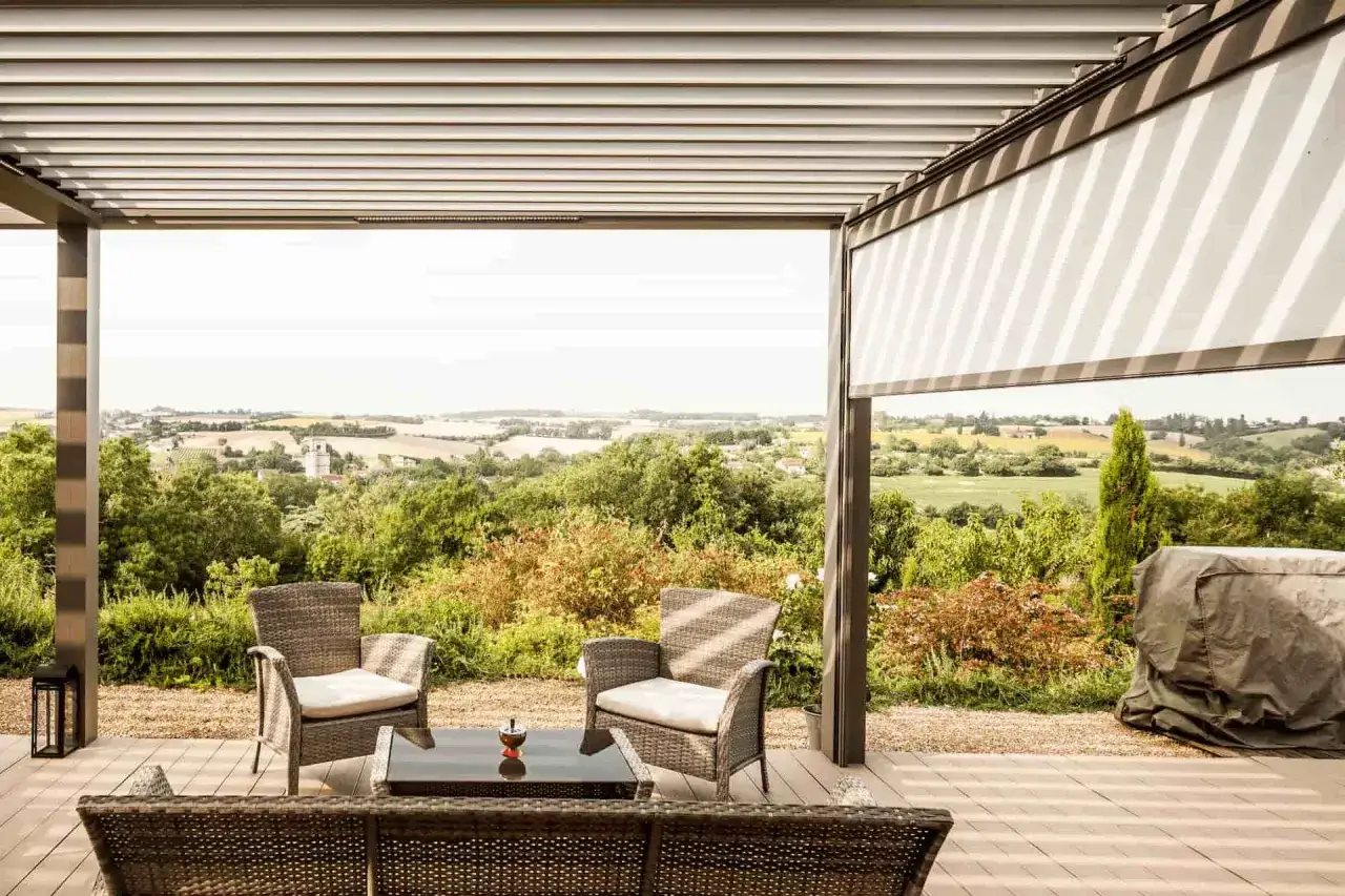 Terrasse aménagée sous une pergola moderne, offrant une vue panoramique sur la campagne. Un fabricant de pergolas de qualité pour profiter de votre extérieur.