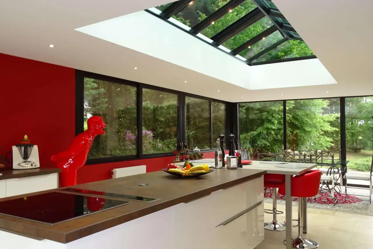 Cuisine moderne avec une veranda puit de lumiere baign&eacute;e de soleil, murs rouges, &icirc;lot central et sculpture audacieuse.