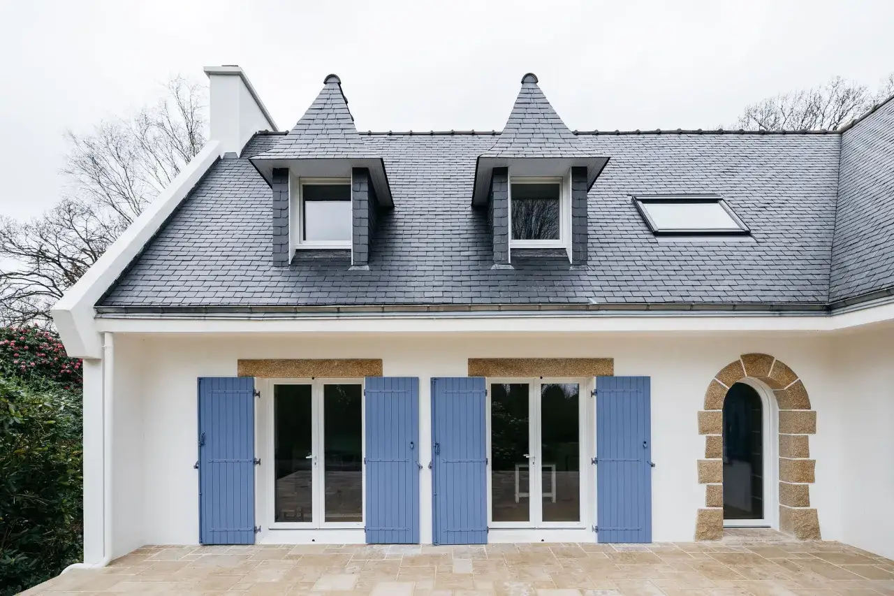 Extension maison n&eacute;o-bretonne avec toiture en ardoise, lucarnes pointues et volets bleus.