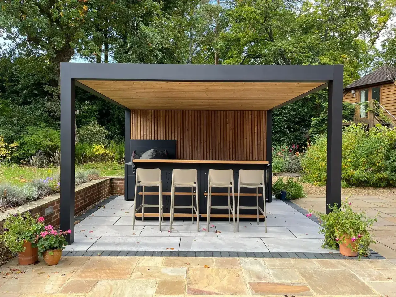 Moderne mod&egrave;le de pergola pour terrasse avec bar ext&eacute;rieur et tabourets. Parfait pour recevoir en plein air.