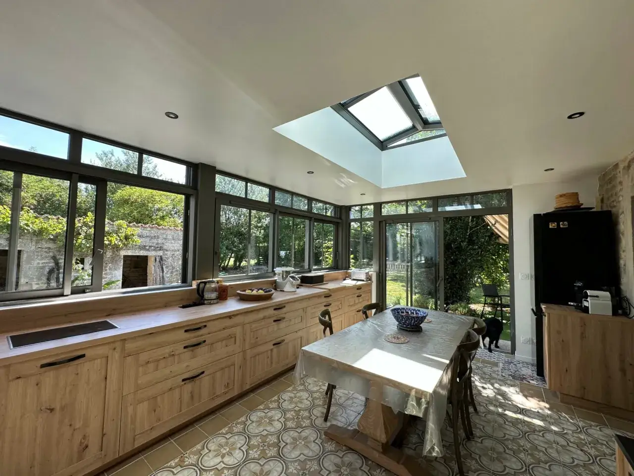 Belle extension cuisine maison avec de grandes fen&ecirc;tres et un puits de lumi&egrave;re, meuble en bois clair, table dress&eacute;e.