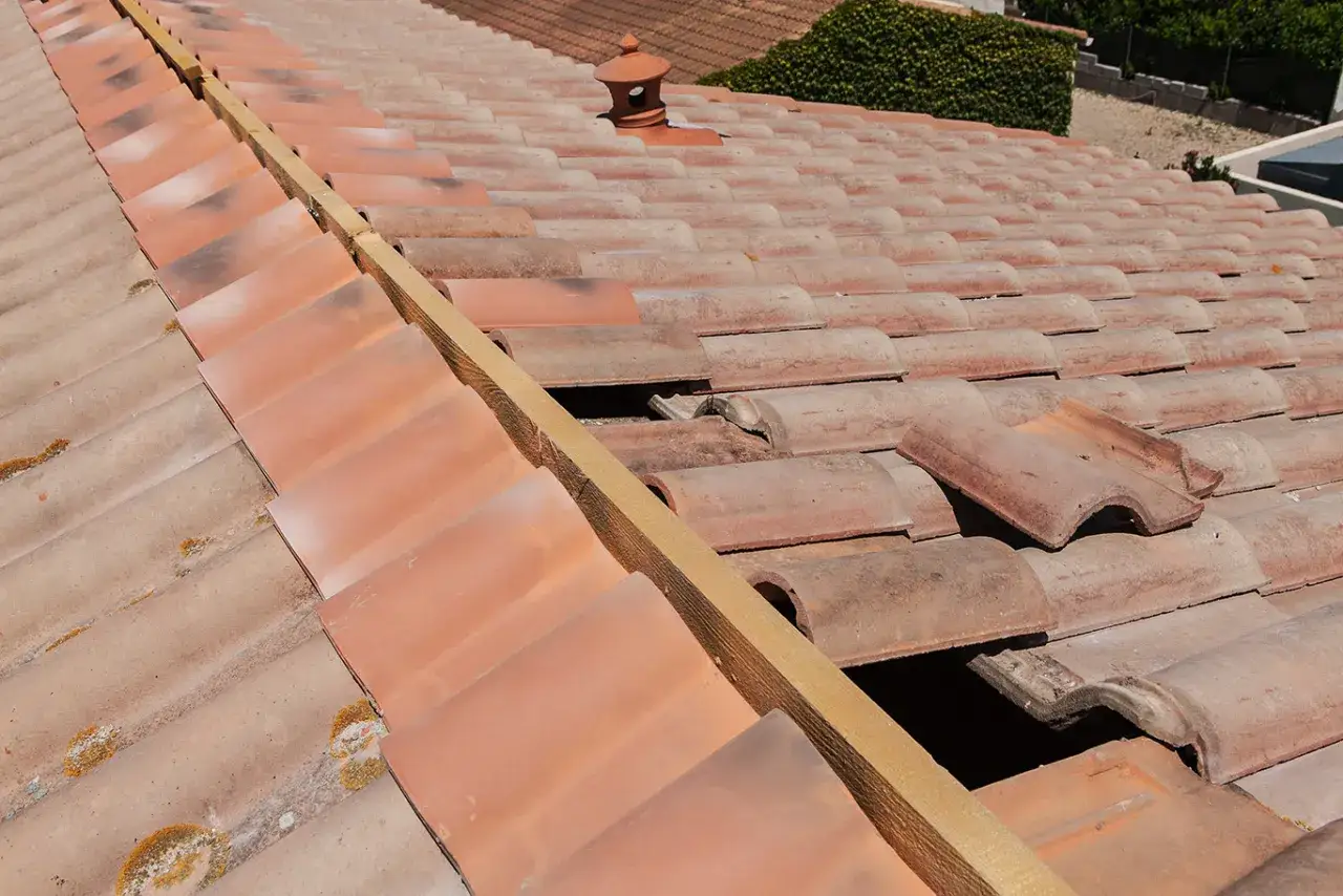 Vue rapproch&eacute;e d'un toit en tuiles anciennes, certaines d&eacute;plac&eacute;es r&eacute;v&eacute;lant un puit de lumi&egrave;re dans une maison ancienne.