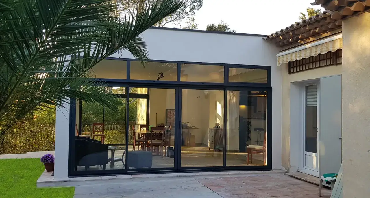 Une extension toit moderne avec de grandes baies vitr&eacute;es donnant sur un jardin luxuriant. L'int&eacute;rieur r&eacute;v&egrave;le une salle &agrave; manger et un salon confortables.