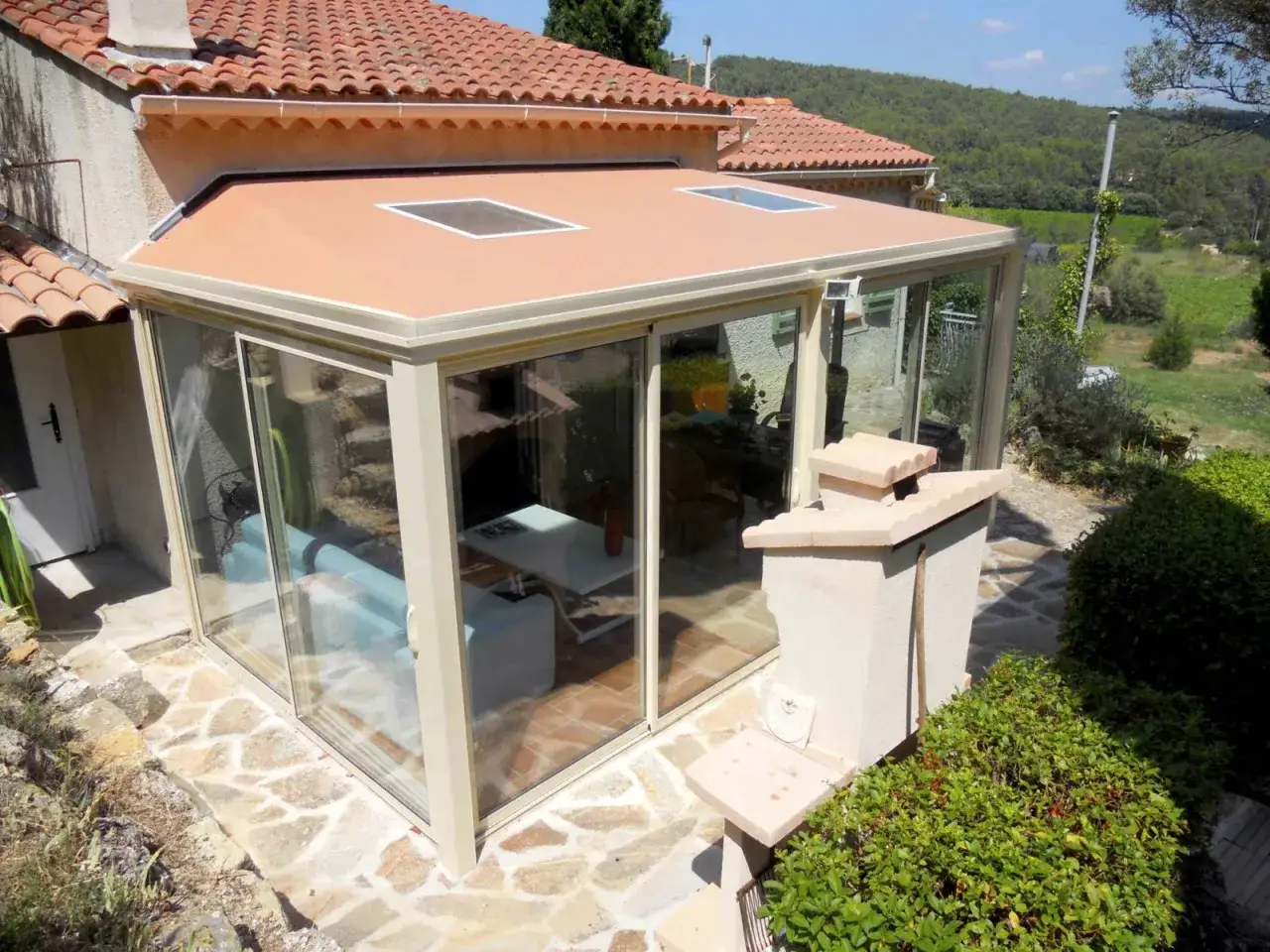 Une veranda tuile moderne avec de grandes baies vitr&eacute;es et deux puits de lumi&egrave;re, offrant une vue sur un paysage verdoyant.