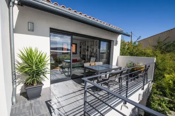 Terrasse sur le toit accessible, avec table et chaises, et une grande baie vitrée donnant sur un salon rempli de livres.