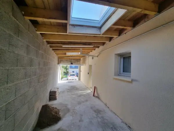 Vue d'une extension en cours de construction avec reprise de toiture, poutres apparentes et un puits de lumière.