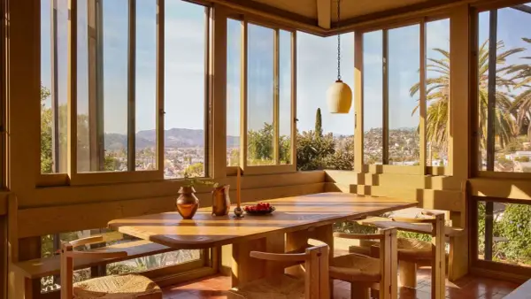 Une salle à manger lumineuse dans une veranda sur terrasse en bois, avec vue panoramique sur la ville et les palmiers.