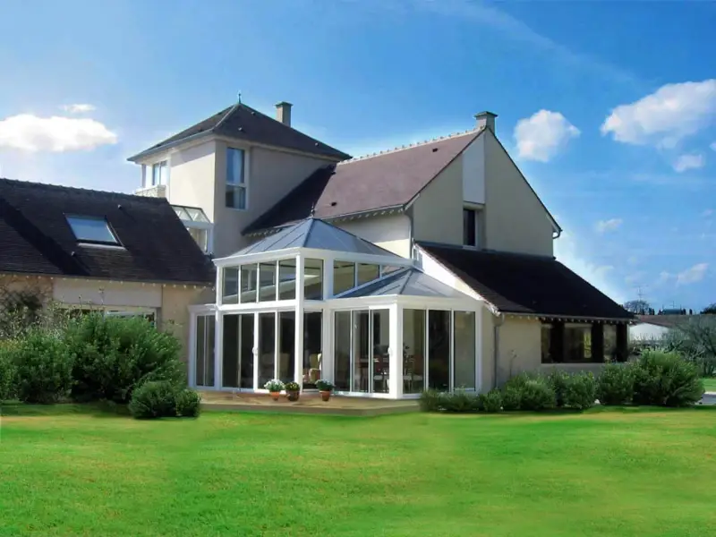 Une **veranda angle maison** moderne, avec une structure vitrée lumineuse, s'intègre parfaitement à l'architecture de la demeure.