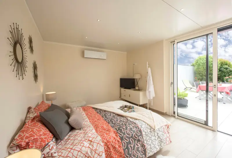 Chambre lumineuse d'une extension de maison, avec un lit confortable, une télévision et un accès direct à une terrasse extérieure.